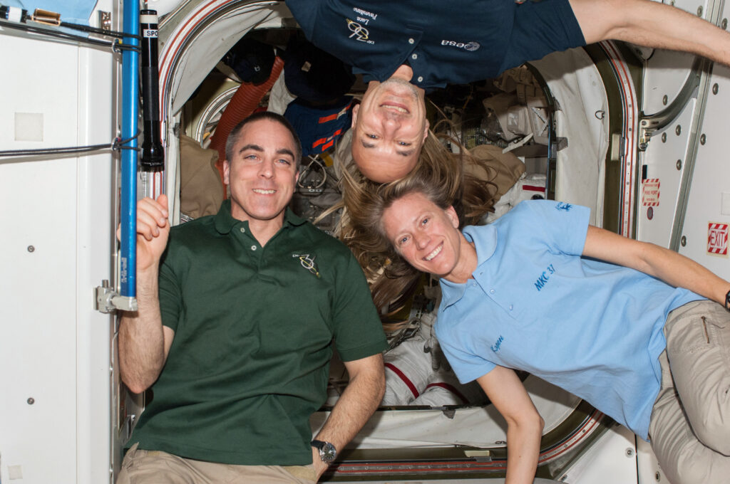 Astronauts Chris Cassidy, Luca Parmitano, and Karen Nyberg on the International Space Station during Expedition 36. The three crew members are floating together in a cabin, oriented at various angles to highlight the weightless environment and team camaraderie of life in space.