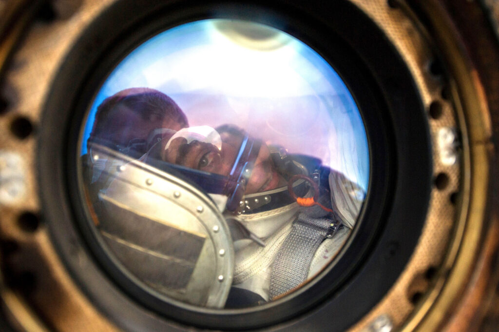 A striking reflection of NASA Astronaut Chris Cassidy’s face seen in a circular porthole aboard the International Space Station, symbolizing the "orbital perspective" and the quiet intensity of living 250 miles above the Earth’s surface.